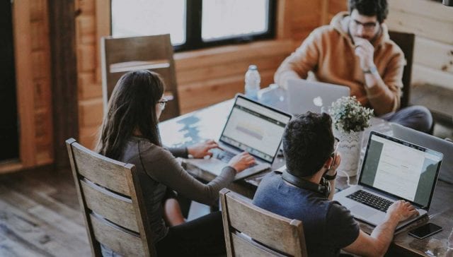 Eine Gruppe von Marketingmitarbeitern arbeitet an Laptops an einem Tisch.