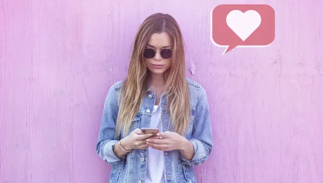 Eine Frau nutzt ein Mobiltelefon für Social-Media-Marketing vor einer rosa Wand.