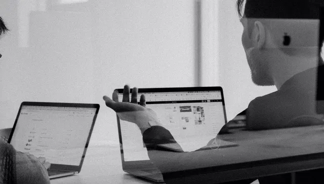 Ein Schwarz-Weiß-Foto, das zwei Personen zeigt, die mit Laptops Wachstumsmarketing-Aufgaben erledigen.