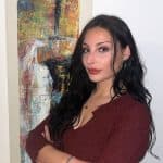 Eine Frau mit dunklem Haar und kastanienbraunem Oberteil steht neben einem abstrakten Gemälde des Einfachmarketing-Teams.