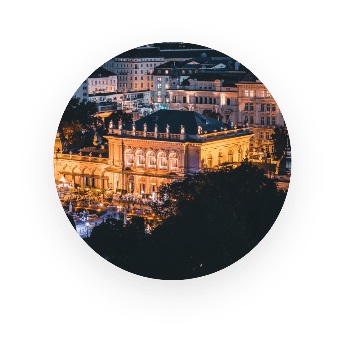 Luftaufnahme eines hell erleuchteten, historischen Gebäudes in einer Stadt bei Nacht, umgeben von anderen beleuchteten Gebäuden.