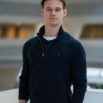 Ein Mitglied des Einfachmarketing-Teams steht in einem schwarzen Pullover mit Viertelreißverschluss im Innenbereich und blickt vor einem weich fokussierten Hintergrund in die Kamera.