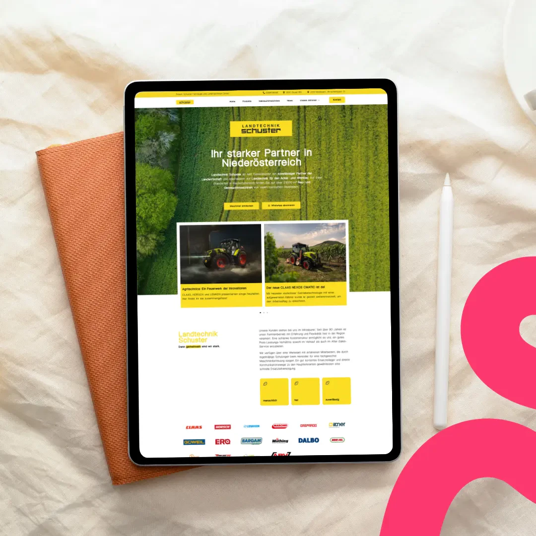 Ein Tablet, auf dem die deutschsprachige Landtechnik Schuster-Website mit Bildern von Traktoren auf einem orangefarbenen Stoff neben einem weißen Stift und einem rosa Grafikelement abgebildet ist.