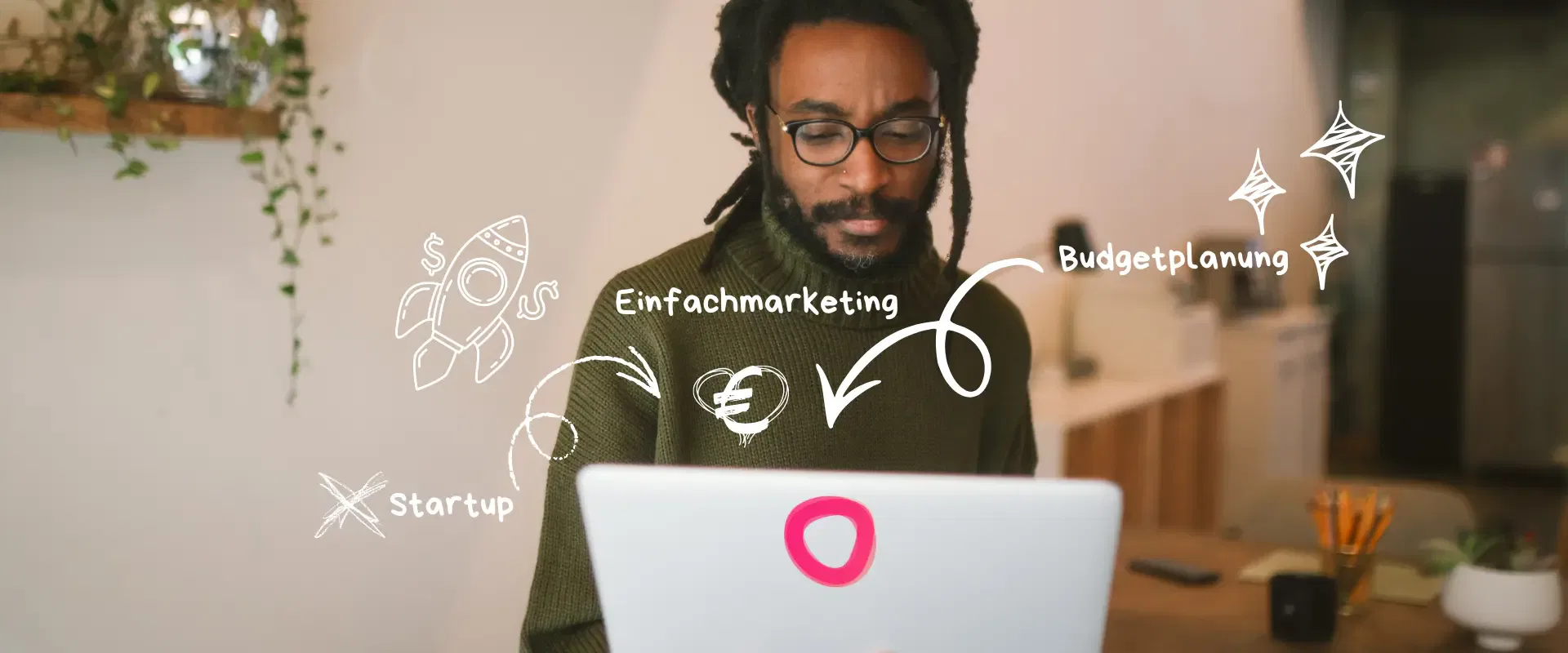 Ein Mann mit Brille arbeitet an einem Laptop, auf dem weiße marketingbezogene Kritzeleien und deutsche Wörter wie 