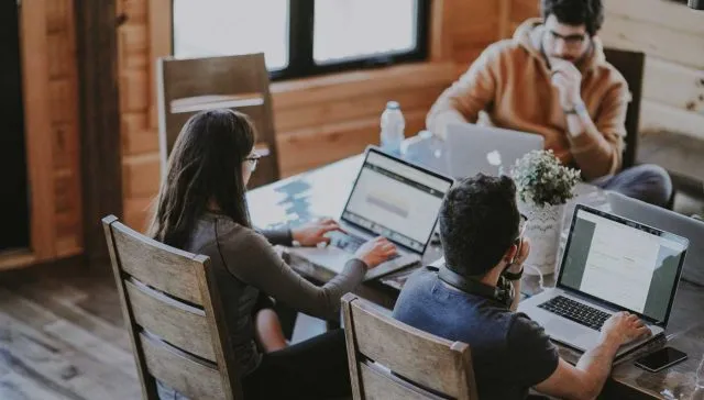 Eine Gruppe von Marketingmitarbeitern arbeitet an Laptops an einem Tisch.