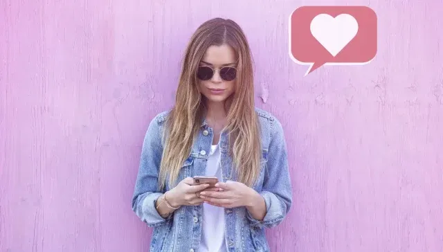 Eine Frau nutzt ein Mobiltelefon für Social-Media-Marketing vor einer rosa Wand.