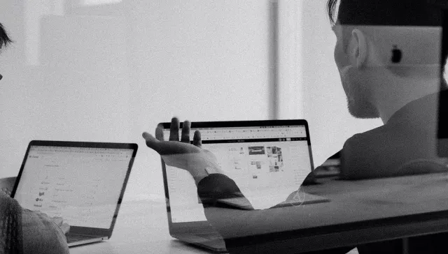 Ein Schwarz-Weiß-Foto, das zwei Personen zeigt, die mit Laptops Wachstumsmarketing-Aufgaben erledigen.