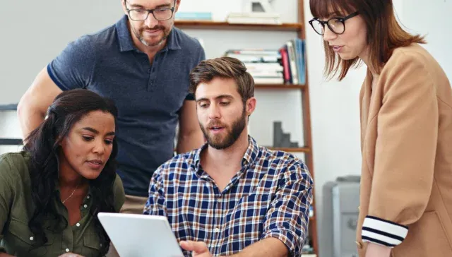 Eine Gruppe von Menschen schaut in einem Büro auf ein Tablet.