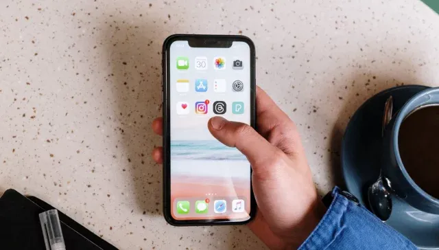 Eine Person hält ein iPhone mit der neuen Instagram-App auf einem Tisch neben einer Tasse Kaffee.