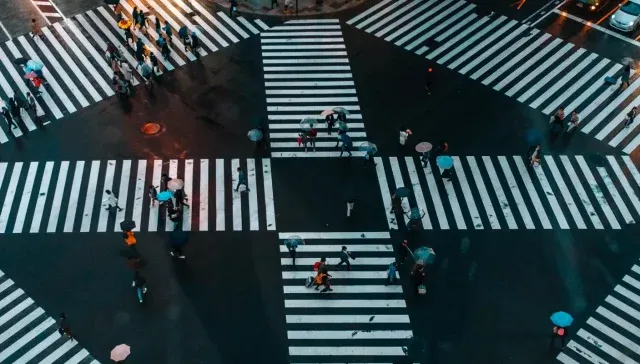 Luftaufnahme eines belebten Fußgängerübergangs mit Menschen, die die Straße in verschiedene Richtungen überqueren, was ein perfektes Szenario für die Zielgruppenanalyse darstellt.