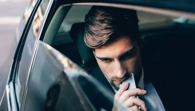 Ein Mann mit ernster Miene blickt auf sein Telefon, während er auf dem Rücksitz eines Autos sitzt und die Customer Journey für sein B2B-Unternehmen analysiert.