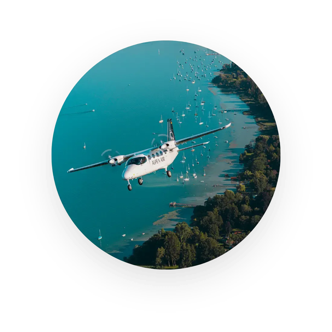 Ein kleines zweimotoriges Flugzeug überfliegt ein Küstengebiet mit zahlreichen im Wasser verankerten Booten und einer grünen Uferlinie.