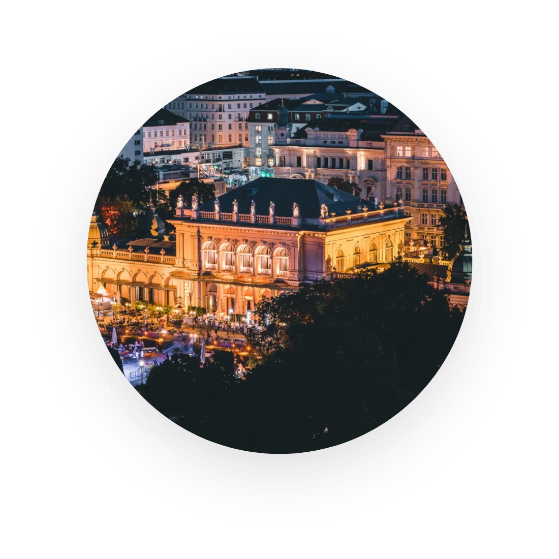 Luftaufnahme eines hell erleuchteten, historischen Gebäudes in einer Stadt bei Nacht, umgeben von anderen beleuchteten Gebäuden.