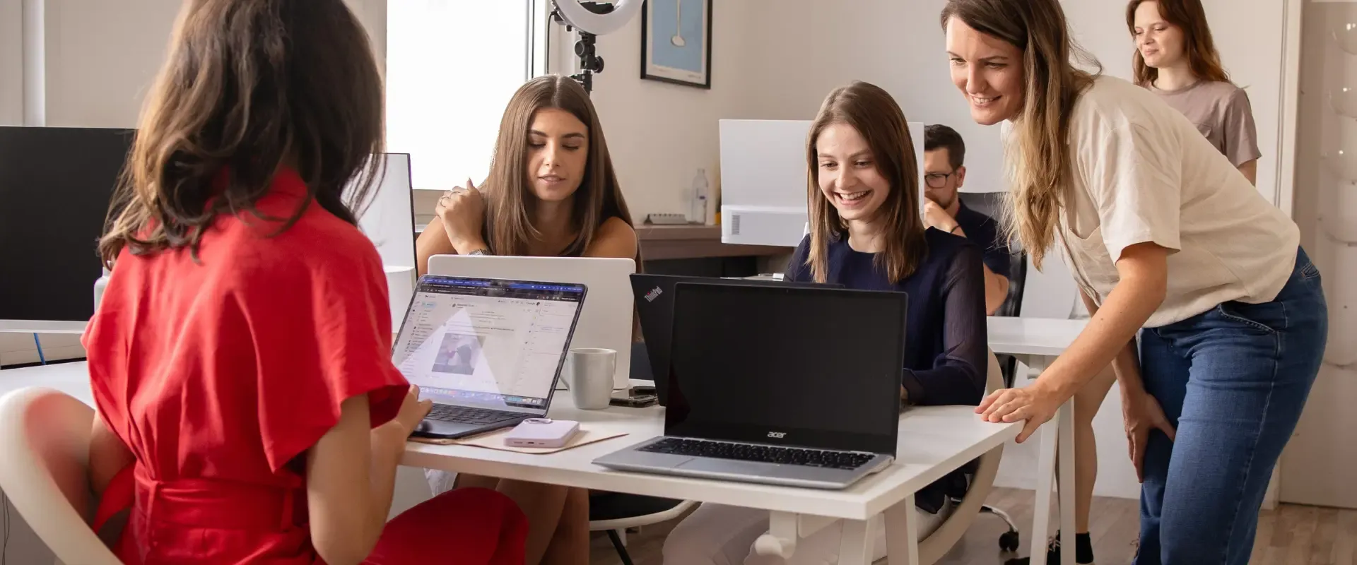 Eine Gruppe von Marketingberatern arbeitet in einer Büroumgebung zusammen und sitzt an einem Tisch an Laptops. Im Hintergrund sind ein Whiteboard und andere Bürogeräte zu sehen.