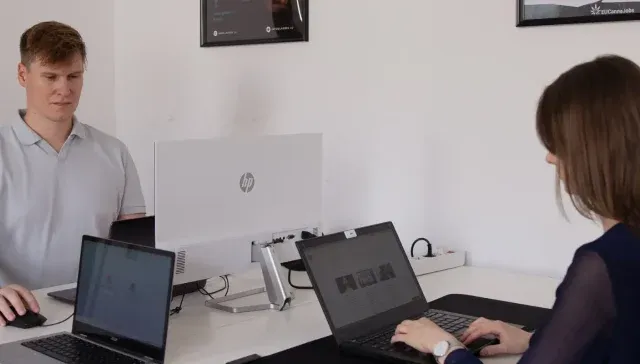 Zwei Personen arbeiten an einem weißen Schreibtisch an Laptops und arbeiten automatisch an einem Projekt zusammen. Jeder von ihnen ist konzentriert und stellt sicher, dass jeder Entwurf und jede gespeicherte Datei perfekt synchronisiert ist, während sie sich zielstrebig gegenüberstehen.