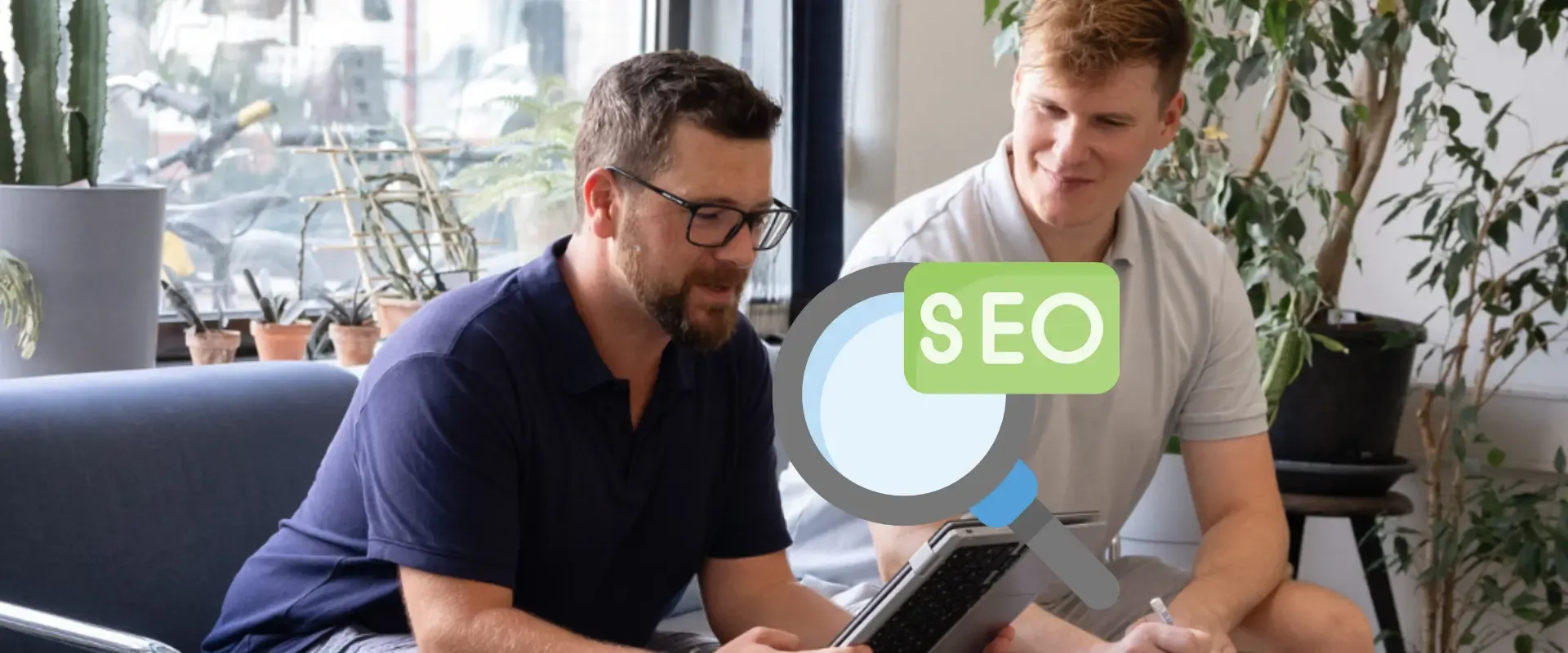Zwei Personen sitzen auf einem Sofa und diskutieren über SEO. Eine Person hält ein Tablet in der Hand. Über das Bild ist eine Grafik einer Lupe mit der Aufschrift „SEO“ gelegt. Dies unterstreicht, wie wichtig es ist, die Suchabsicht zu verstehen, um Suchabsichtsstrategien effektiv zu verbessern.