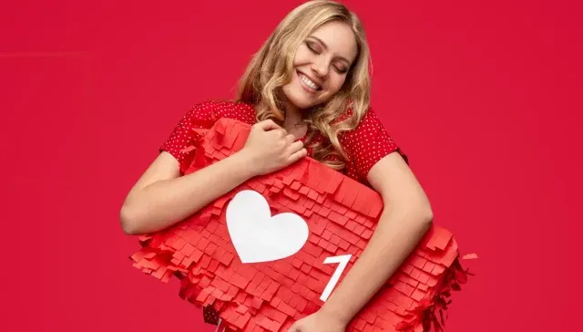 Eine lächelnde Person umarmt vor einem roten Hintergrund eine herzförmige Piñata und fängt damit die Essenz von Leidenschaft und Kreativität ein, ähnlich den dynamischen Strategien des Social Media Marketing.