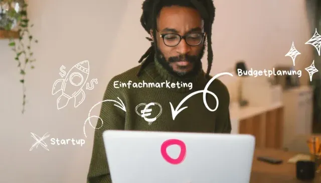 Ein Mann mit Brille arbeitet an einem Laptop, auf dem weiße marketingbezogene Kritzeleien und deutsche Wörter wie 