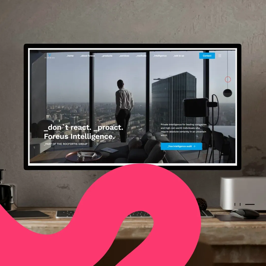 Ein Computermonitor auf einem Schreibtisch zeigt eine Foreus-Fallstudien-Website mit einer Person, die an einem großen Fenster mit Blick auf eine Stadtlandschaft steht. Im Vordergrund ist eine rosa abstrakte Form zu sehen.